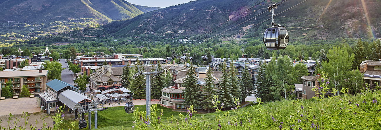 The Little Nell hotel at the base of Aspen Mountain and the Silver Queen Gondola on a blue-sky summer day.