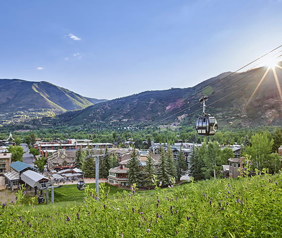 The Little Nell hotel at the base of Aspen Mountain and the Silver Queen Gondola on a blue-sky summer day.