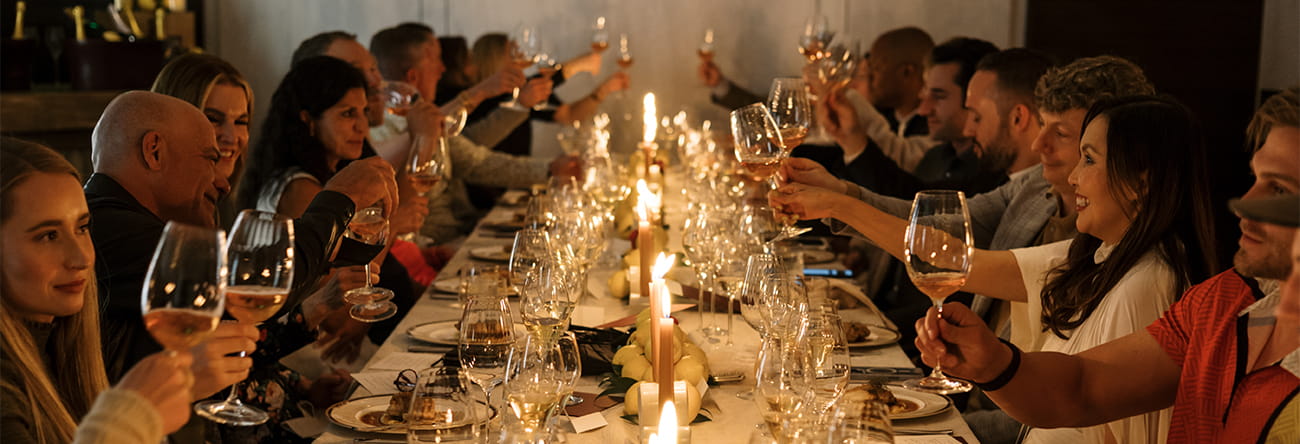 A group of guests toasting their glass of wine at a candle lit table.