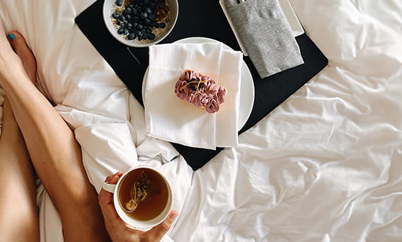 Breakfast in bed with a pastry, oats, and cup of coffee.