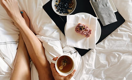 A guest relaxing in bed with a cup of coffee, pastry, and bowl of oats. 