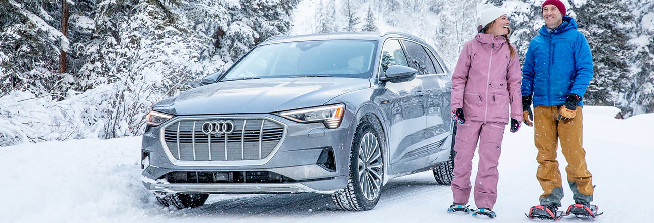 A couple stands next to an Audi about to venture on a snowshoe tour.