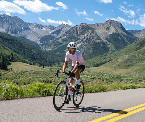 A cyclist riding down the road with blue skies and green mountains in the background.