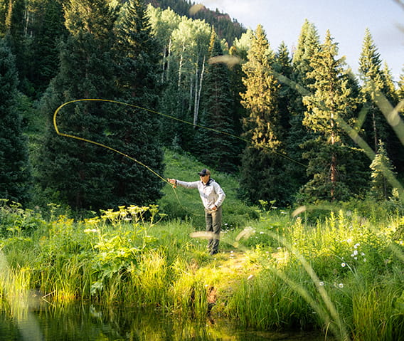 A man in a green meadow fly fishing.