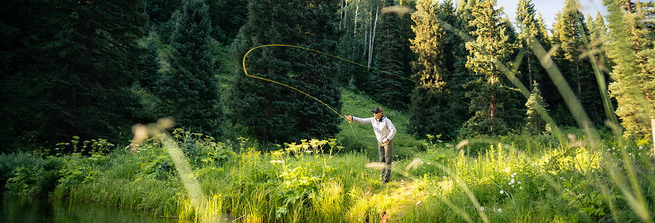 A man in a green meadow fly fishing.
