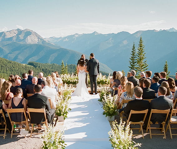 A bride and groom at the top of Aspen Mountain during their ceremony with the Elk Mountain Range in the background.