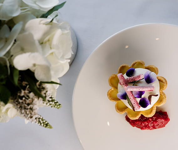 A tartlet covered in purple edible flowers accompanied by a strawberry.