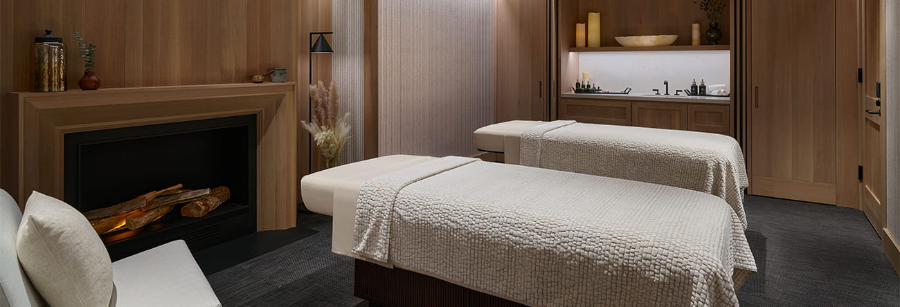 A private treatment room in The Little Nell spa with two massage tables and a fireplace.