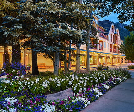 The Little Nell sidewalk with storefronts and flower beds in the evening.