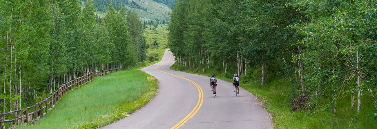 Two people riding bikes in the Roaring Fork Valley with mountains in the horizon.