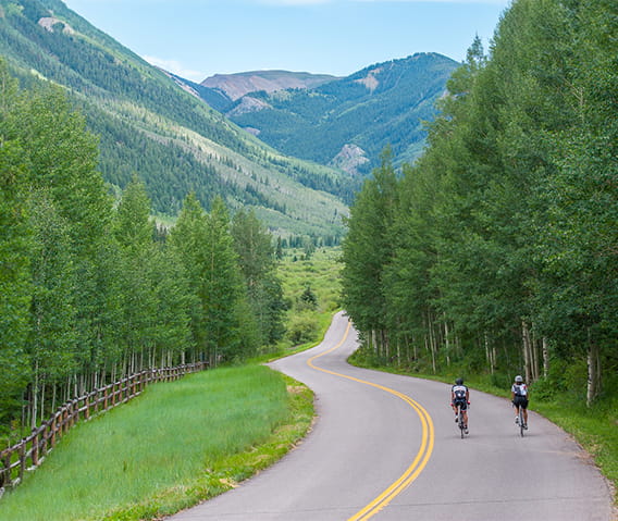 Two people riding bikes in the Roaring Fork Valley with mountains in the horizon.