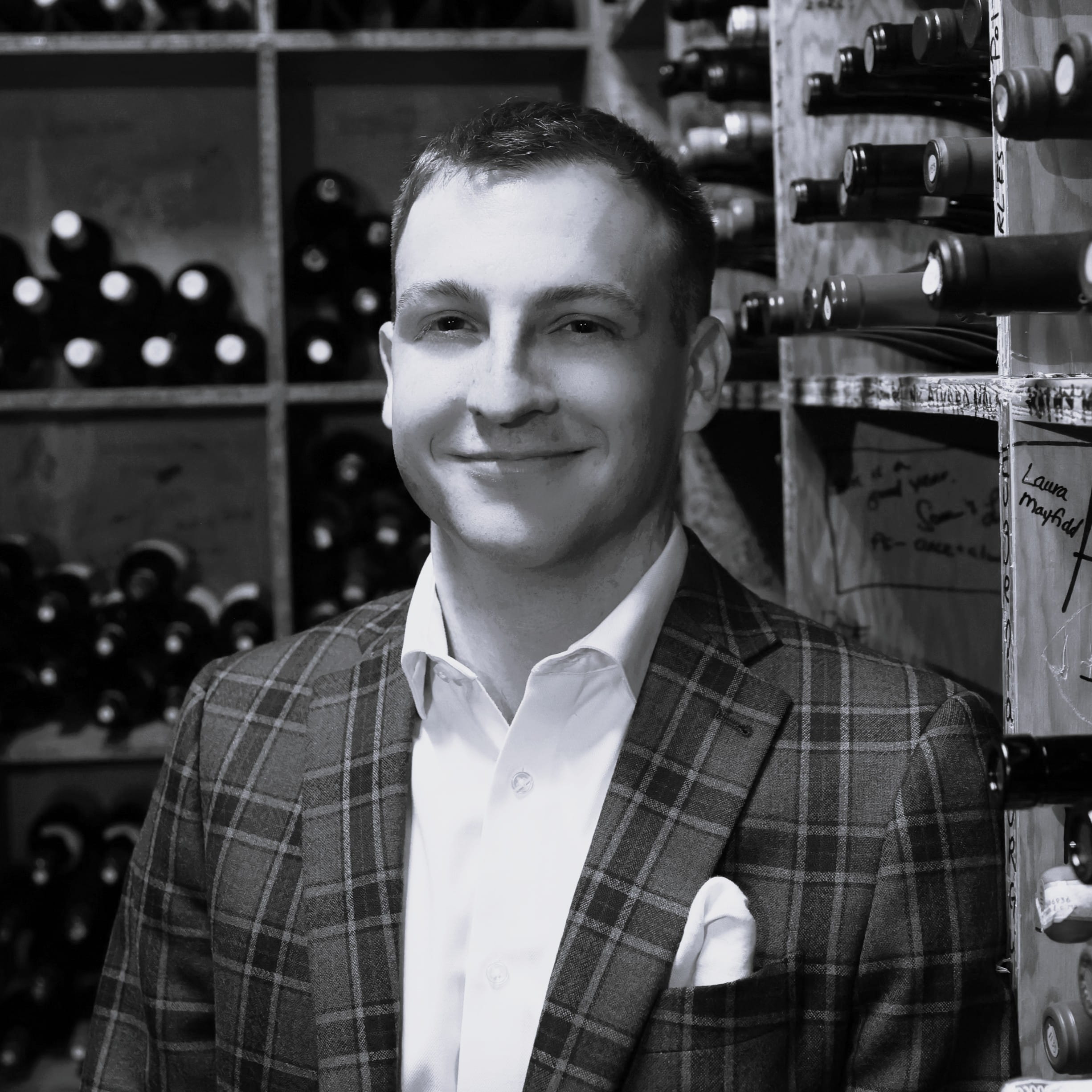 black & white headshot of a man wearing a suit in a wine cellar