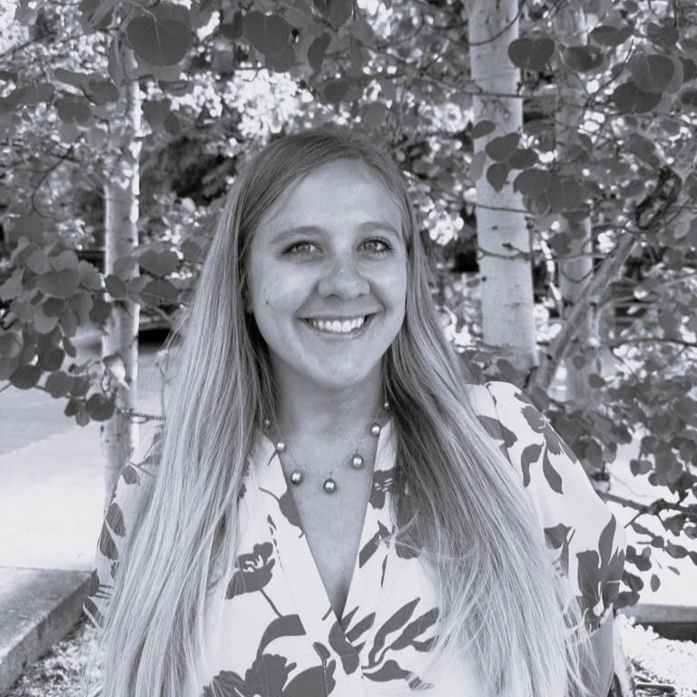 Photo of a woman standing against some trees, in black & white