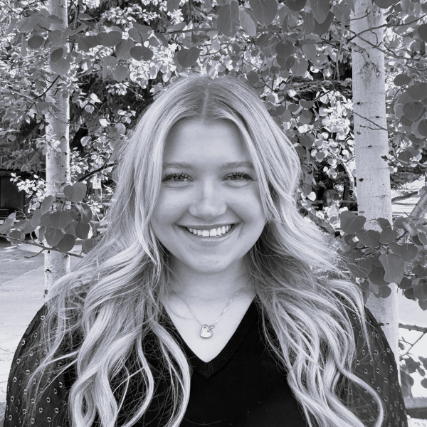 Headshot of a woman with curled blonde hair and a black top against some trees