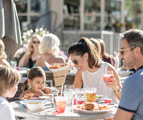 A family enjoys lunch on Ajax Tavern's sunny, mountainside patio at the base of Aspen Mountain.