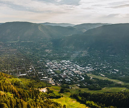 Birds eye view of the town of Aspen with mountains covered in greenery in the background. 