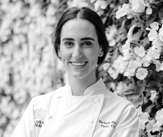 The Little Nell Pastry Chef, Barbara Marcos, in her chef coat in front of a flower wall.