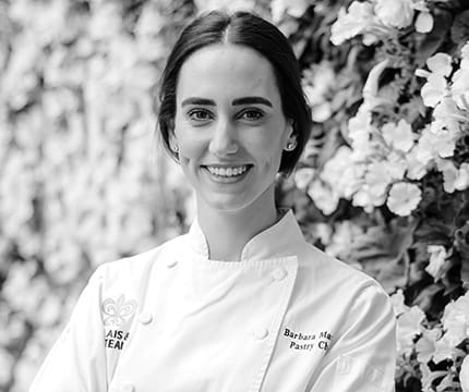 The Little Nell Pastry Chef, Barbara Marcos, in her chef coat in front of a flower wall.