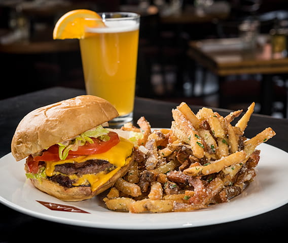 Cheeseburger next to a beer with an orange slice and AJAX Tavern menu.