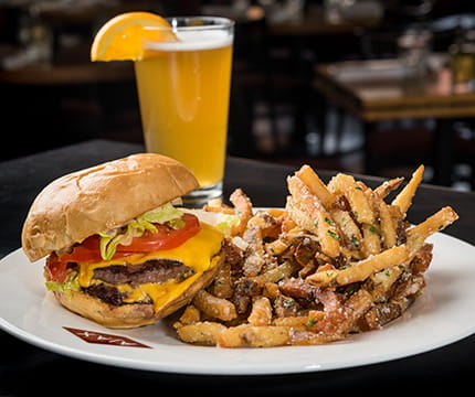 Cheeseburger next to a beer with an orange slice and AJAX Tavern menu.