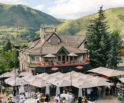 Ajax Tavern exterior with umbrellas and green mountains in the background. 