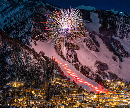 Fireworks lighting up the snow covered Aspen Mountain at night.
