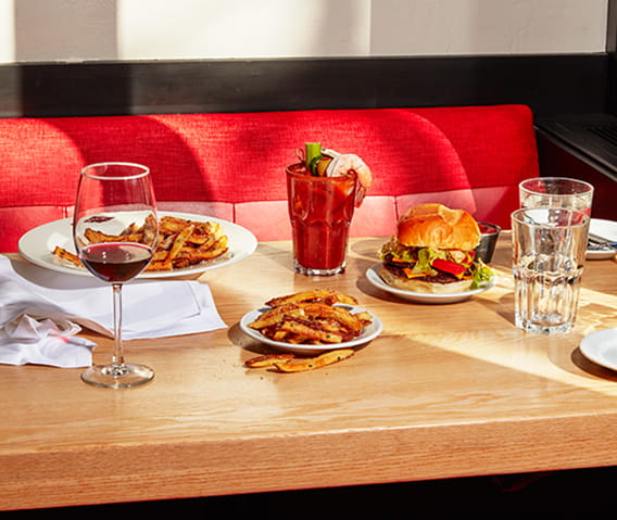 Booth at Ajax Tavern with fries, double cheeseburger, wine, and a bloody mary on the table.  
