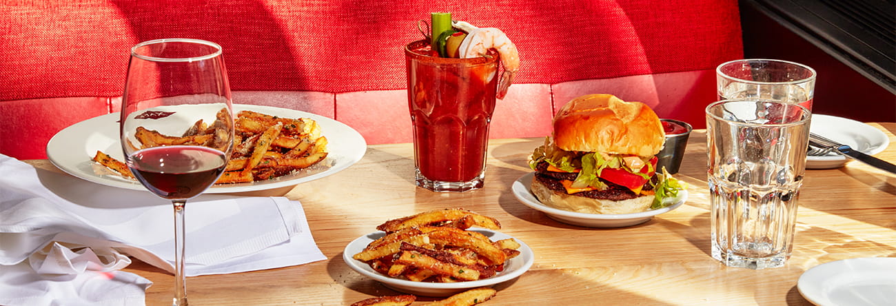 Booth at Ajax Tavern with fries, double cheeseburger, wine, and a bloody mary on the table.  