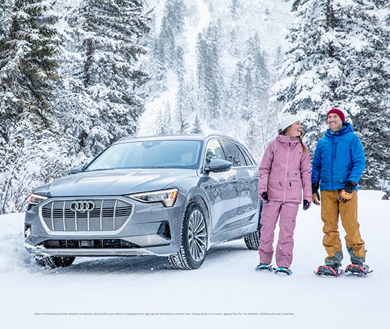 A couple stands next to an Audi about to venture on a snowshoe tour.