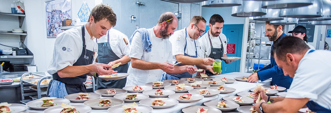 Participating chefs in The Little Nell Culinary Fest preparing many dishes in the kitchen.