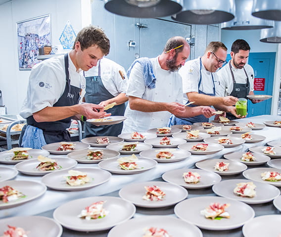 Participating chefs in The Little Nell Culinary Fest preparing many dishes in the kitchen.