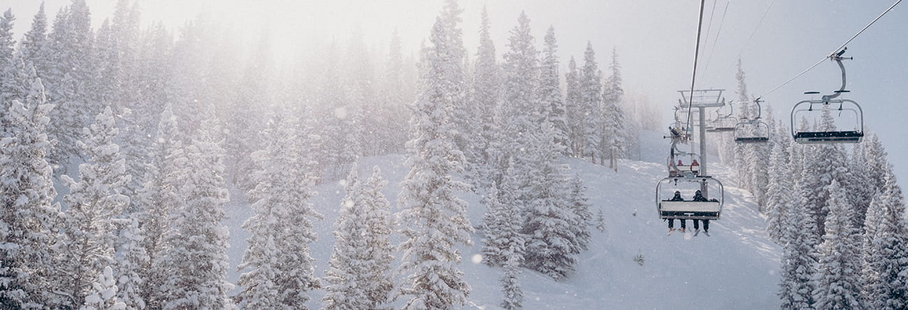 The sillhouette of two skiiers riding up the chairlift with snow falling around them.