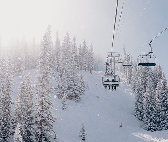 The sillhouette of two skiiers riding up the chairlift with snow falling around them.