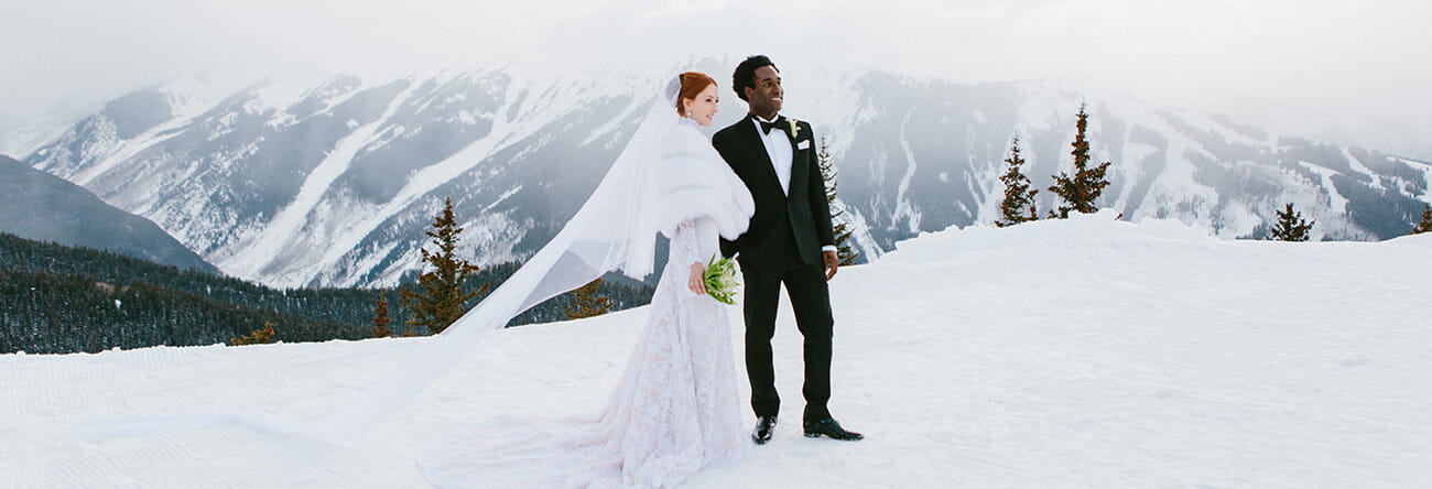 A couple stands on top of Aspen Mountain before their wedding ceremony, surrounded by snow-capped peaks.