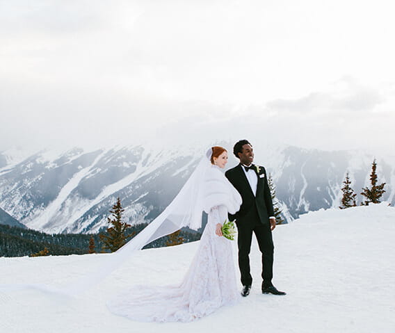 A couple stands on top of Aspen Mountain before their wedding ceremony, surrounded by snow-capped peaks.