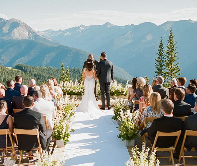 A bride and groom at the top of Aspen Mountain during their ceremony with the Elk Mountain Range in the background.