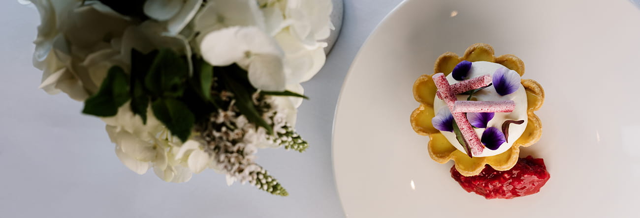 A tartlet covered in purple edible flowers accompanied by a strawberry.