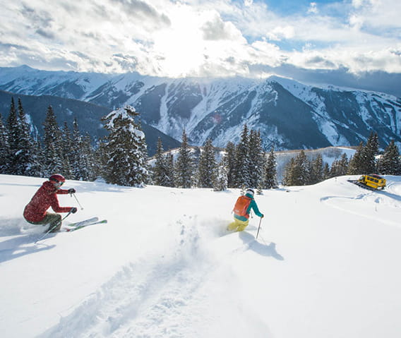 Two skiiers on untouched powder skiing towards their private snow cat.