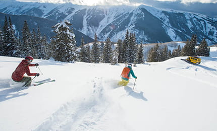 Two skiiers on untouched powder skiing towards their private snow cat.