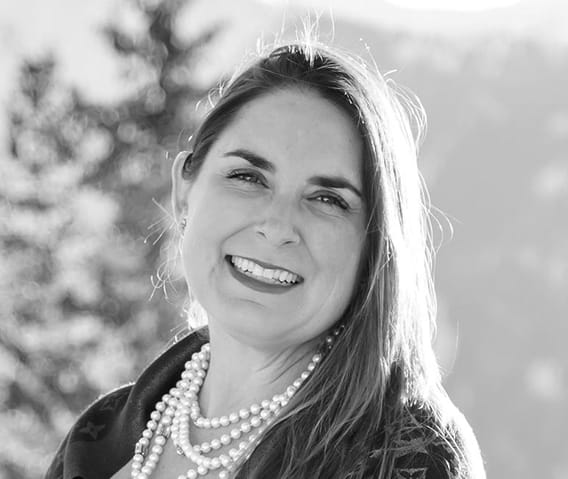 Black and white headshot of Senior Events Sales Manager, Melina Glavas Chandy with mountain peaks in the background.