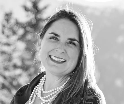 Black and white headshot of Senior Events Sales Manager, Melina Glavas Chandy with mountain peaks in the background.