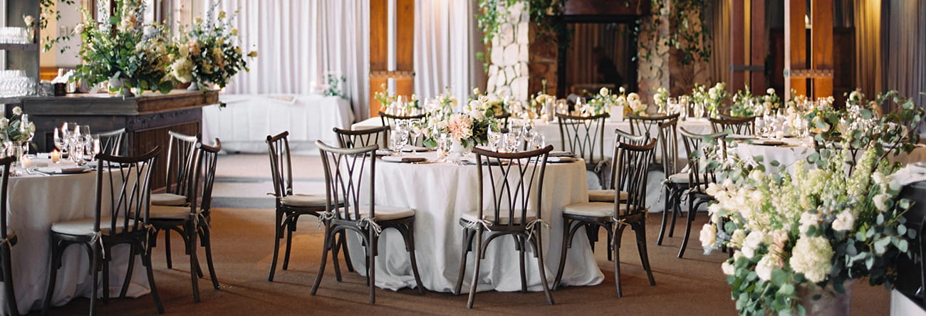 Tables set for a wedding reception dinner inside the sundeck with greenery and white floral decorations.