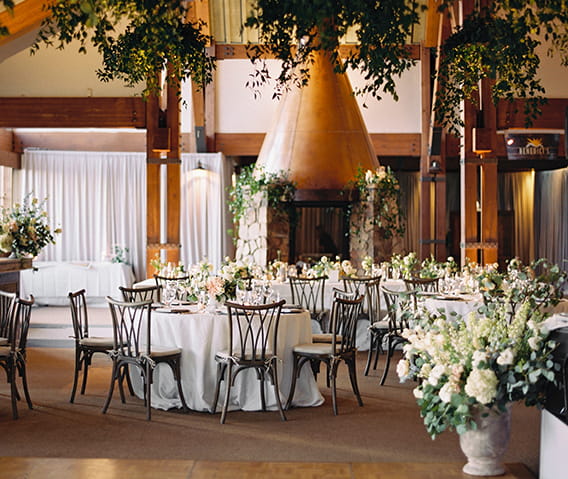Tables set for a wedding reception dinner inside the sundeck with greenery and white floral decorations.