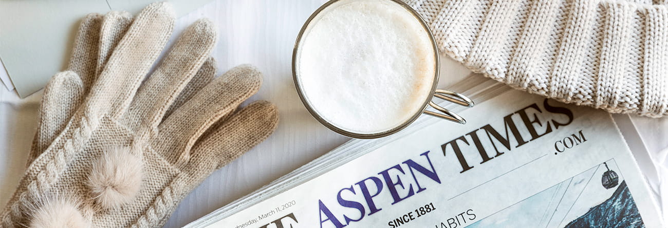 Winter gloves, a latte, a beanie, and The Aspen Times Newspaper on a table.