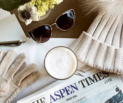 Winter gloves, a latte, a beanie, and The Aspen Times Newspaper on a table.