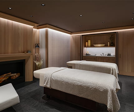 A private treatment room in The Little Nell spa with two massage tables and a fireplace.