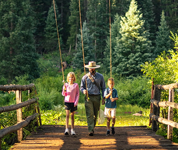 Fly fishing guide and two children walking across a bridge with their fishing poles in hand.