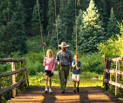 Fly fishing guide and two children walking across a bridge with their fishing poles in hand.