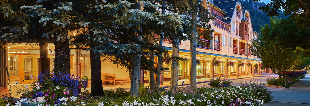 The Little Nell sidewalk with storefronts and flower beds in the evening.