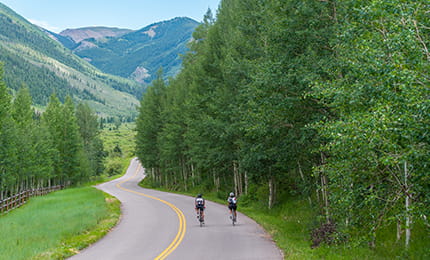 Two people riding bikes in the Roaring Fork Valley with mountains in the horizon.